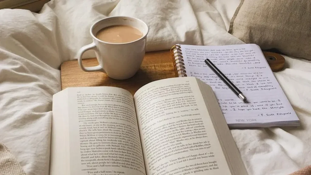 Imagem com um livro, caderno e xícara de café para ilustrar a leitura